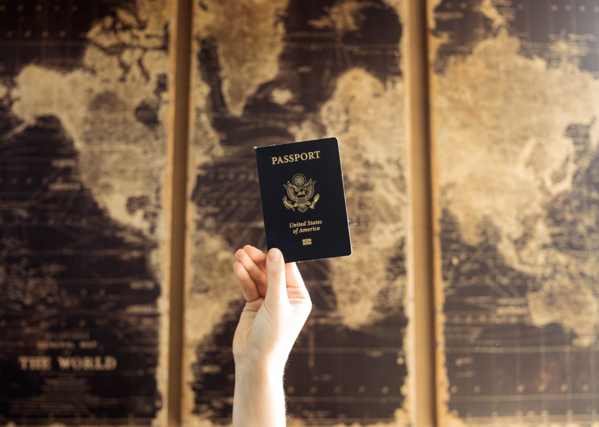 mano che tiene un passaporto americano sullo sfondo di una mappa del mondo vintage