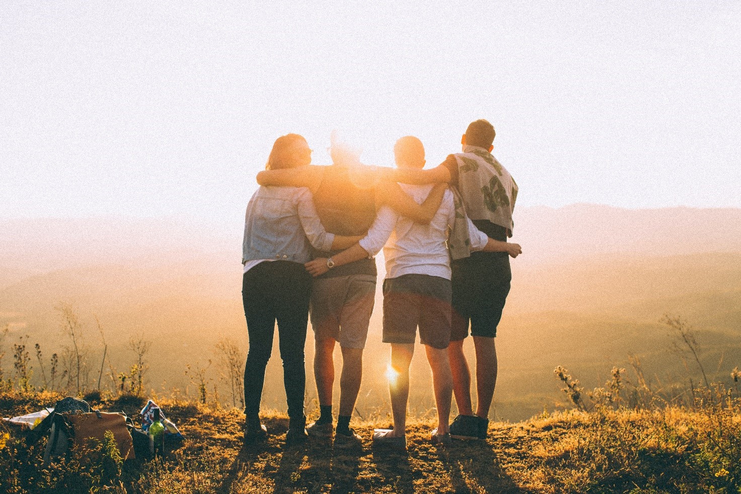quattro amici di spalle si abbracciano mentre guardano il tramonto